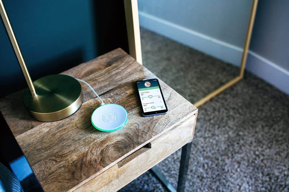 Nightstand with Owlet monitor and phone showing monitoring screen on it.