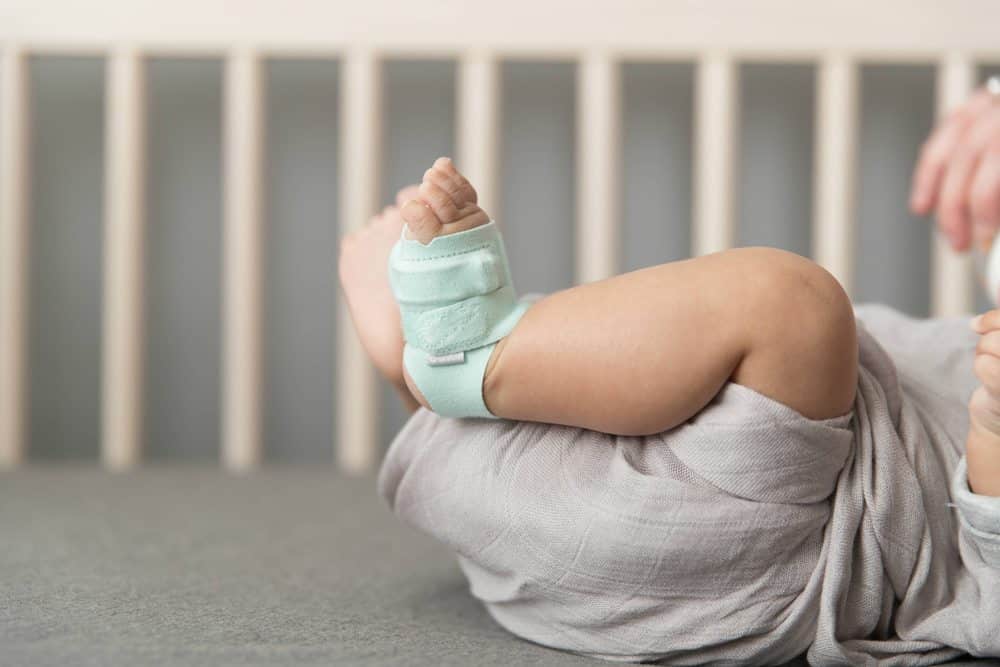 Baby laying in crib with Owlet dream sock on their foot