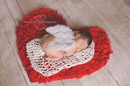 Newborn sleeping on red heart rug with angel wings on their back