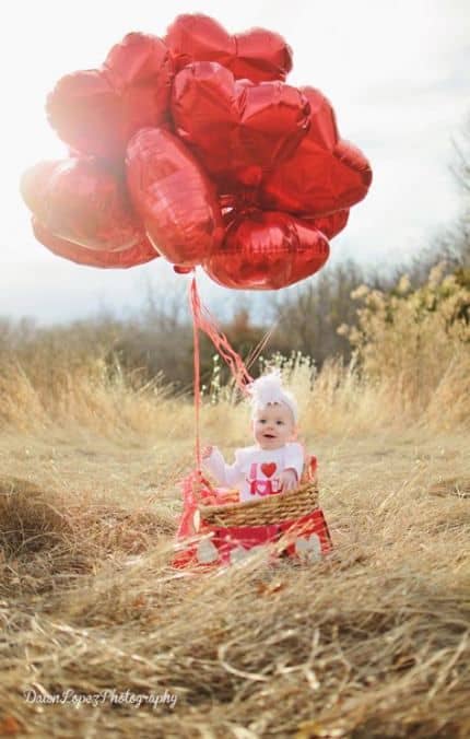 Baby in a field with red heart balloons