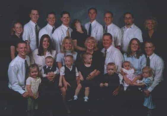 Family photo featuring many people standing in rows with pregnant woman passed out in the back center row