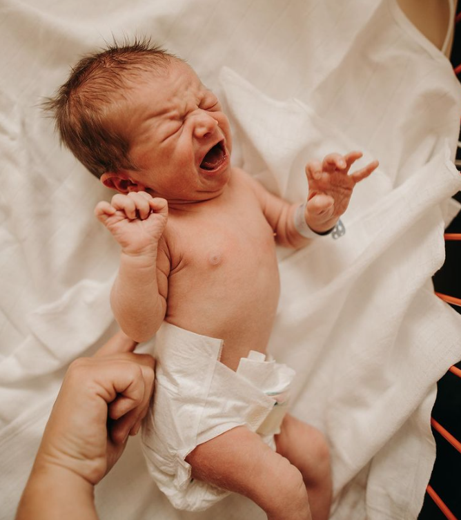 Color photo of newborn wearing nothing but a diaper, crying.