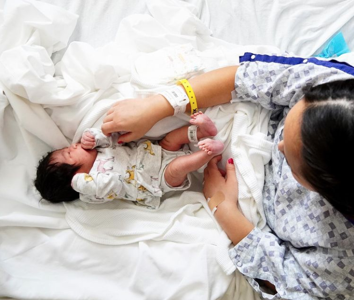 Color photo from above showing mom looking down at newborn laying in her lap.