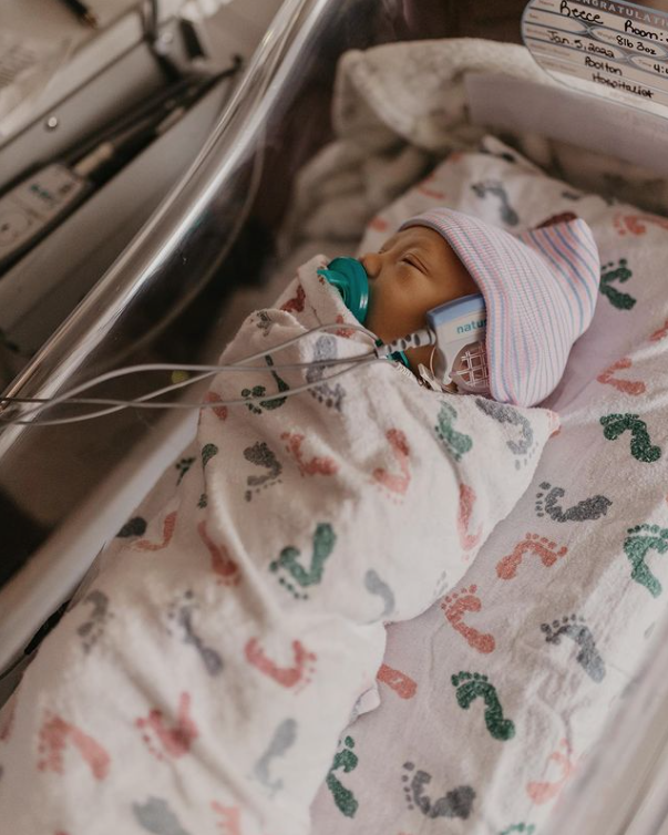 Color photo of swaddled baby using a pacifier and receiving a hearing test in the hospital bassinet. 