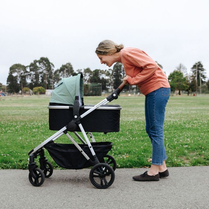 Profile of mom smiling down into Mockingbird bassinet on a stroller in the park