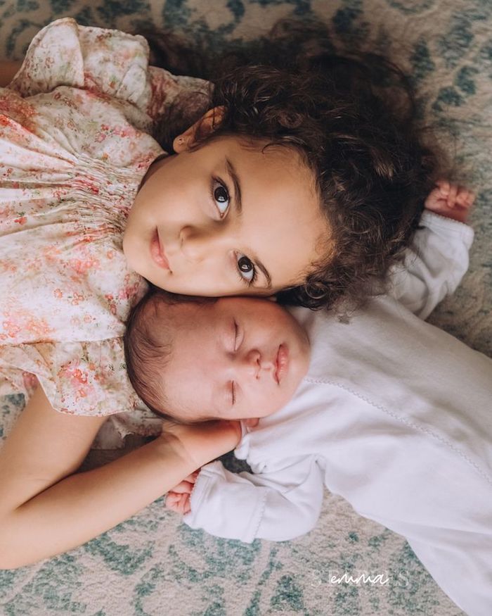 Kid sister with newborn baby sibling posed on carpet looking at camera