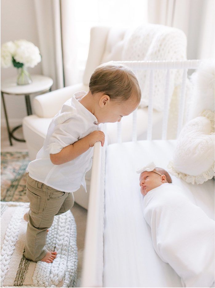 Toddler big brother looking over crib at new baby sister