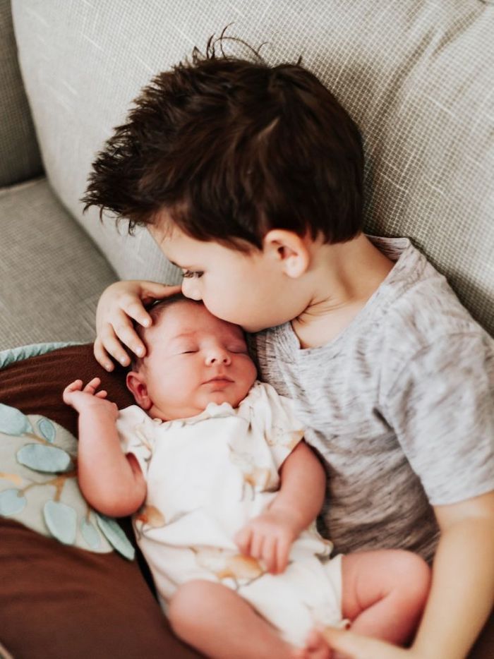 Big brother kissing new baby sibling while sitting on a chair