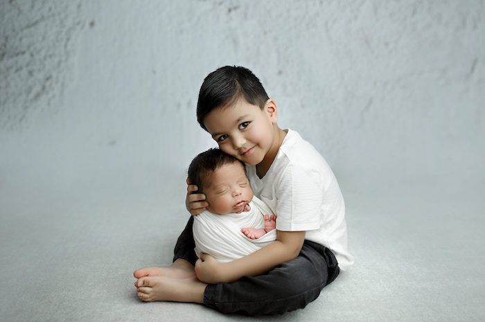 Kid brother holding newborn baby in white swaddle