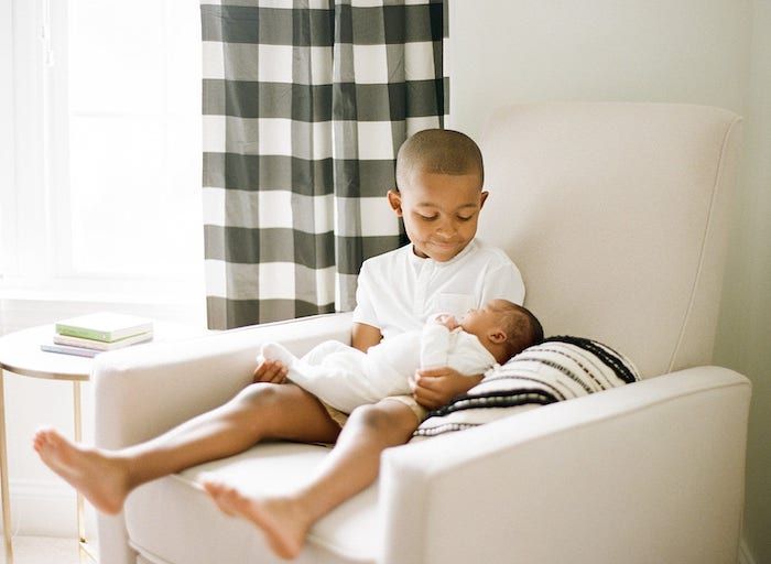 Big brother sitting in nursery chair holding new baby sibling