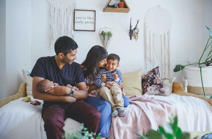 Family posing at home mom with toddler big brother dad holding newborn baby sibling