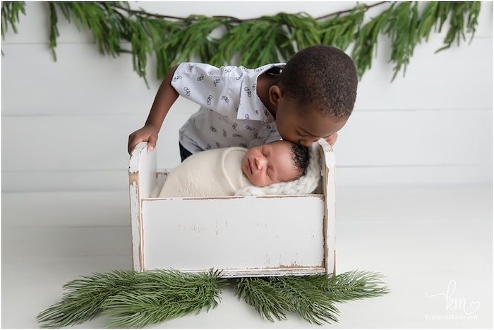 Big brother giving new baby sibling a kiss while swaddled 