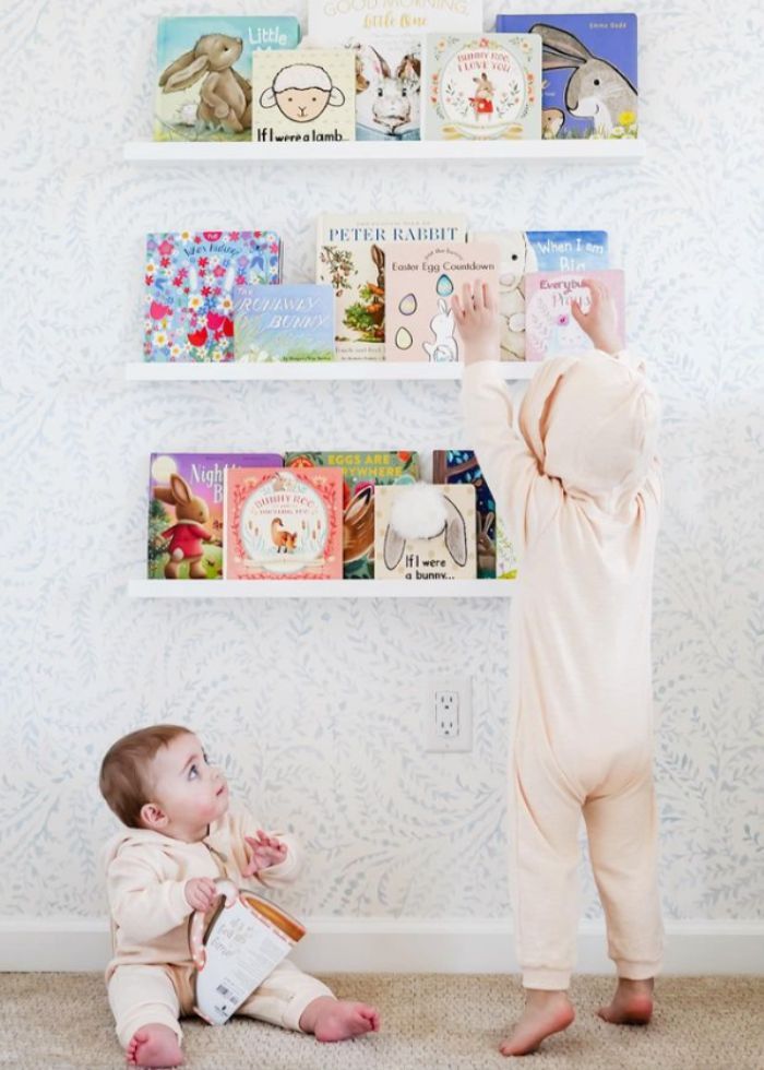 siblings dressed in bunny outfits looking at easter board books on shelves